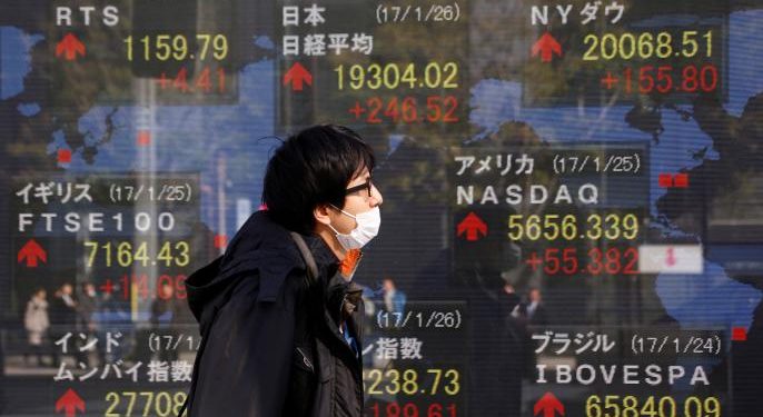 A man walks past an electronic board showing Japan's Nikkei average (top L), the Dow Jones average (top R) and the stock averages of other countries' outside a brokerage in Tokyo, Japan, January 26, 2017.  REUTERS/Kim Kyung-Hoon